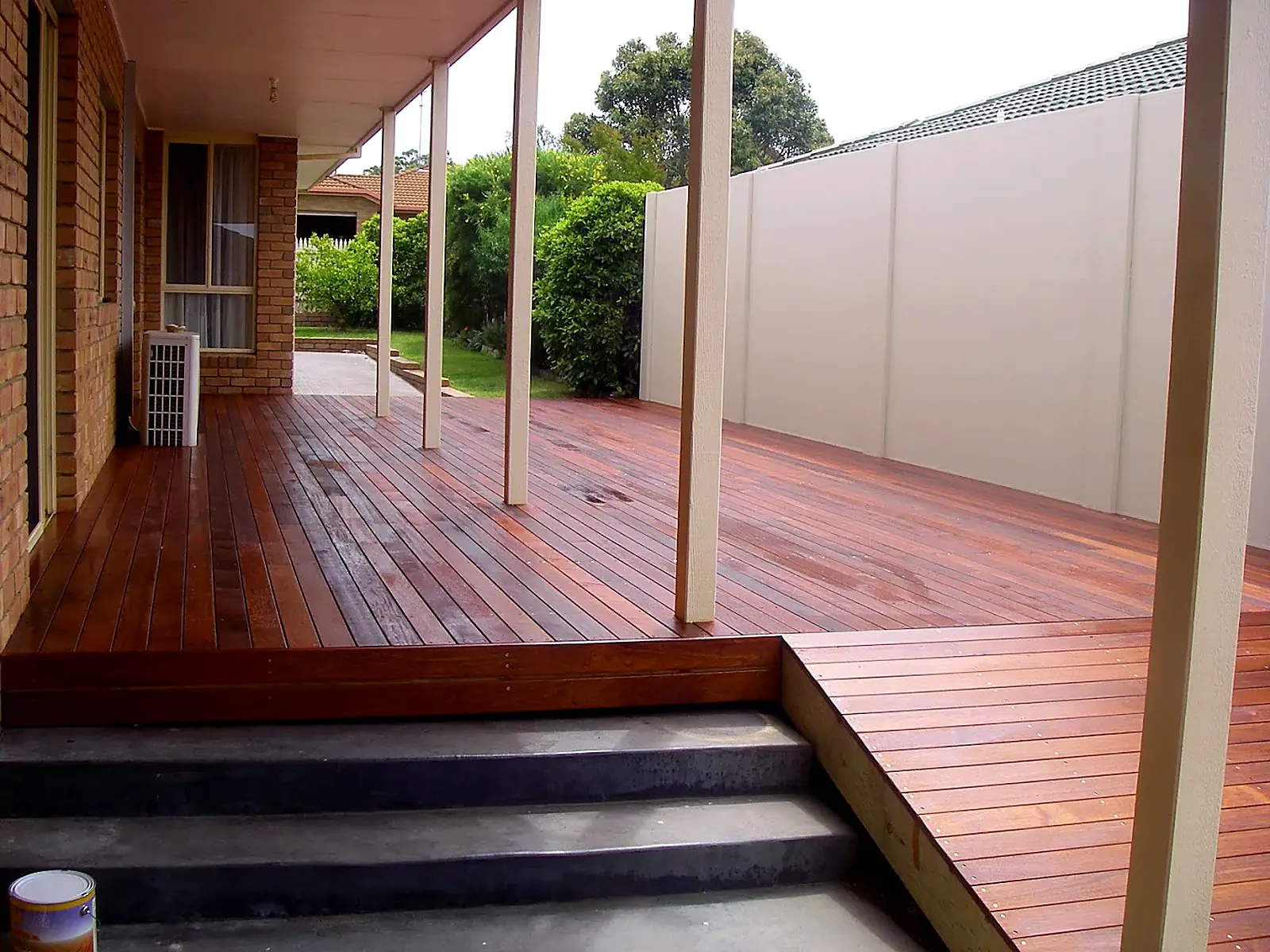 Wrap-around timber deck with cream posts beside a brick home, East Gippsland
