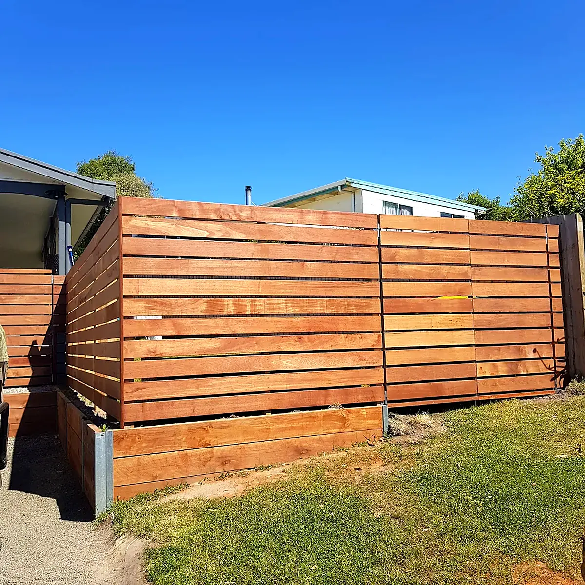 Horizontal timber slat fence and raised garden bed under a blue sky