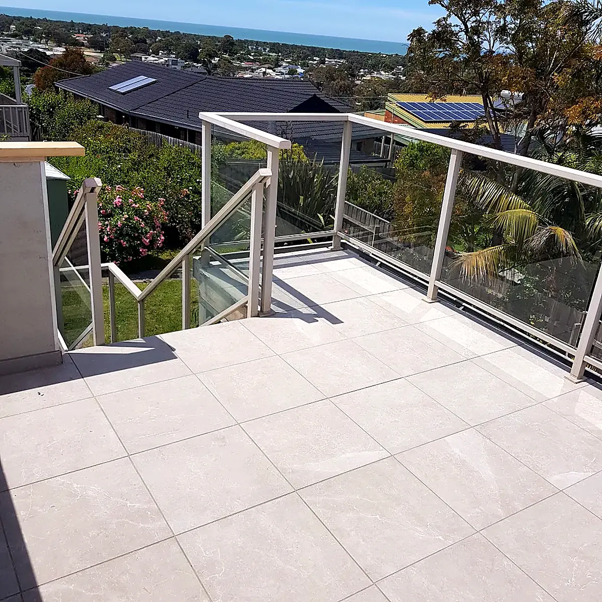 Elevated tiled terrace with glass balustrade and stairs overlooking the coast